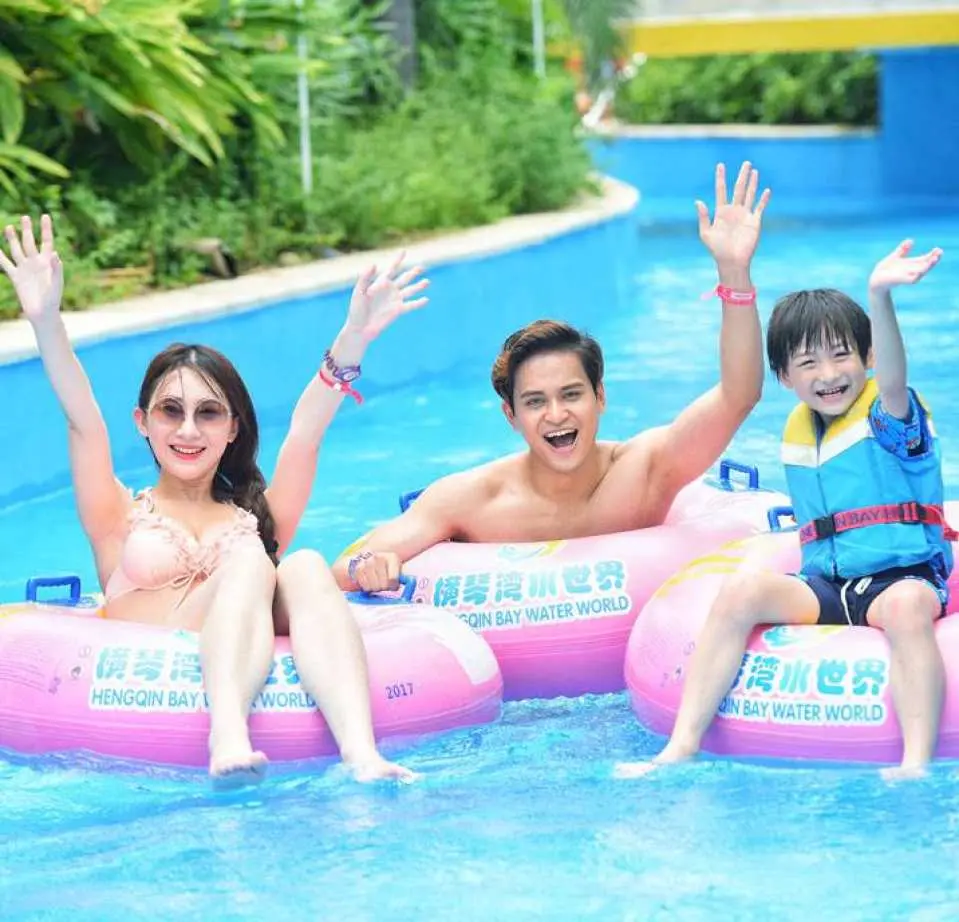 兩位大人與一位小朋友在橫琴灣水世界的漂漂河上，開心地乘坐粉色充氣泳圈，享受輕鬆的水上設施。
