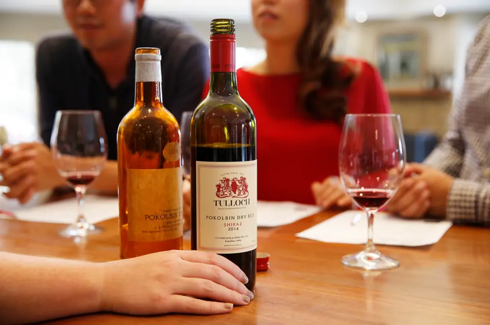 Tulloch Wines Pokolbin Dry Red Shiraz and another varietal bottle, with a wine glass, displayed on a wooden table during a private tasting session in New South Wales.