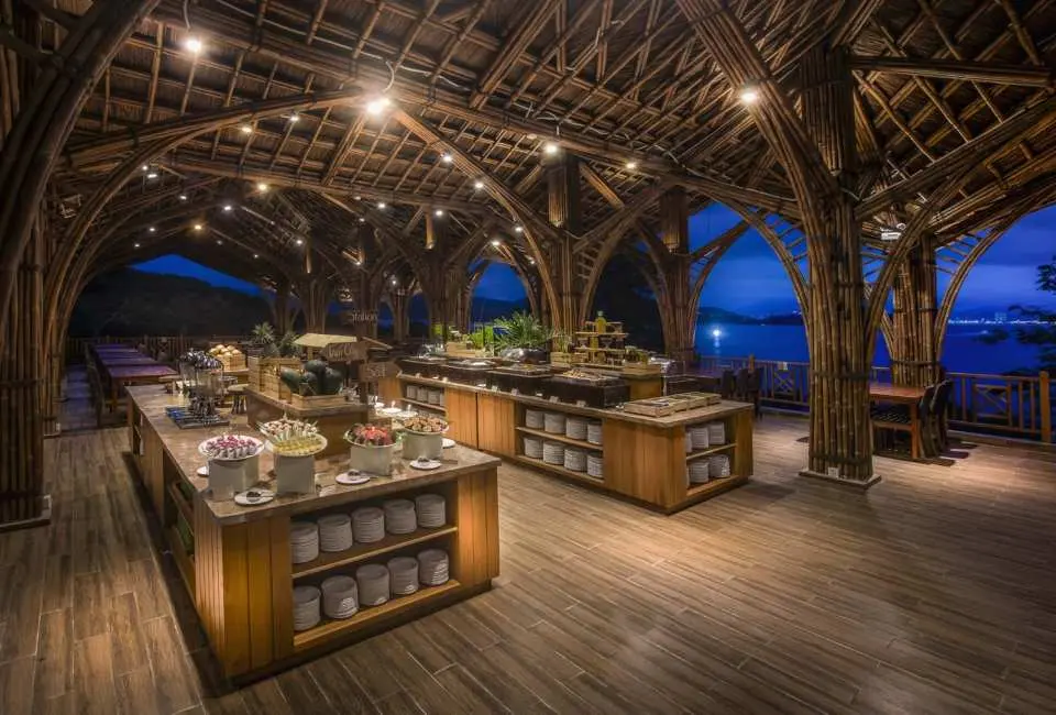 Night view of Soul Viet Restaurant at Hon Tam Island, Nha Trang, with unique bamboo arched ceilings glowing under warm lighting, a ready buffet area, and beautiful bay views.