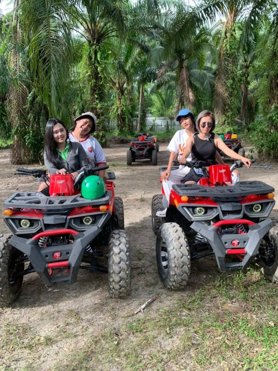 A group of friends smiling and posing on red ATV quad bikes on a dirt path amidst lush tropical palm trees in Krabi, Thailand, enjoying a jungle adventure.