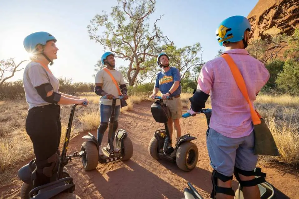 Small group of adventurers gathered with their Segways on a red dirt path, preparing for an immersive guided tour around Uluru's sacred base.