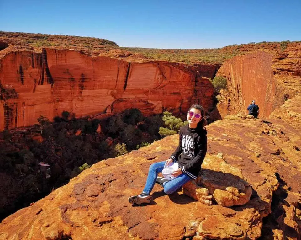 A visitor relaxing on a rocky outcrop at Kings Canyon's rim, gazing out at the expansive red gorge landscape of Watarrka National Park.