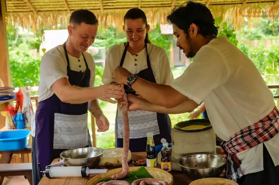 At a Northern Thai cooking school in Chiang Mai, an instructor guides students in making traditional Sai Oua sausage, a Lanna specialty, experiencing hands-on culinary craftsmanship.