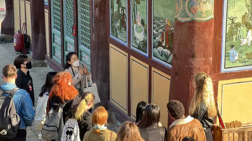 Visitors at a historic Daegu temple attentively observing colorful Buddhist murals on its traditional walls, immersing themselves in the rich local culture and heritage.