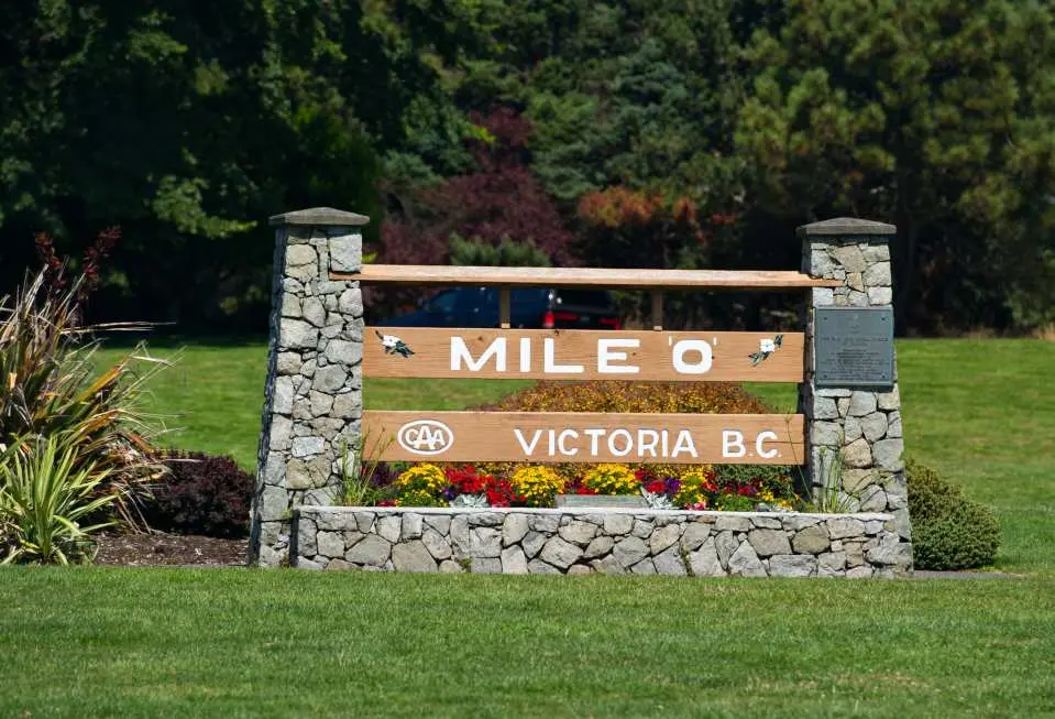 Victoria's famous Mile 0 highway landmark, a wooden and stone sign adorned with flowers and green grass, marking the Trans-Canada Highway's starting point, a must-visit on a chartered day tour.