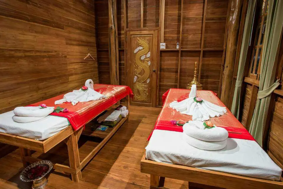 Serene couples massage room within Grace Spa Pattaya's traditional teak wood house, featuring two neatly prepared beds with elegant swan towel decorations.