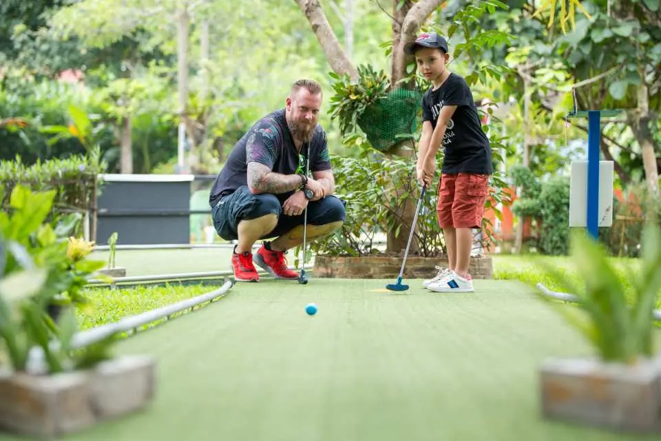 タイのチェンマイX-Centreミニゴルフで、大人が子供にゴルフの打ち方を辛抱強く指導し、心温まる親子時間を楽しんでいます。
