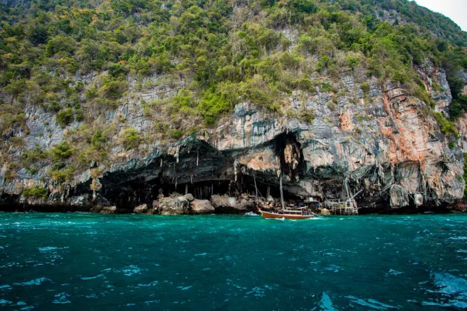 A speedboat sailing past the famous Viking Cave on Phi Phi Island, a dramatic sea cave carved into towering limestone cliffs, during a Phuket island hopping tour.