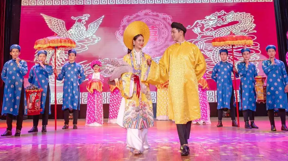 Buổi biểu diễn Áo Dài Đà Nẵng tái hiện vẻ đẹp vương giả của Việt Nam, với các diễn viên trong trang phục cung đình sang trọng màu vàng và xanh-đỏ, trên nền hoa văn rồng phượng uy nghi, tạo nên không khí lịch sử trang trọng và thanh lịch.