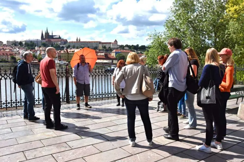 Tourists gathered at a scenic viewpoint, enjoying panoramic views of Prague Castle and the Vltava River, led by a guide on their exciting city tour.