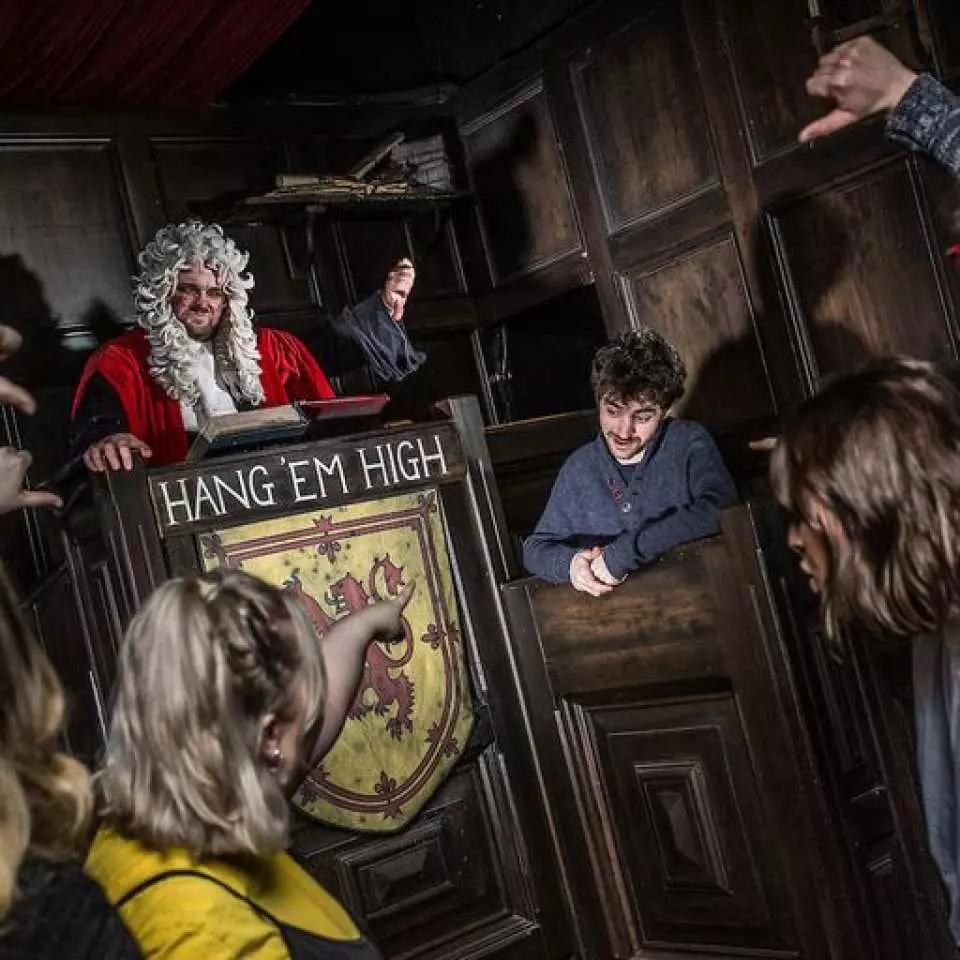 Live actor as a menacing judge at 'Hang 'Em High' show, engaging visitors in a dark historical court scene with theatrical sets at The Edinburgh Dungeon, UK.