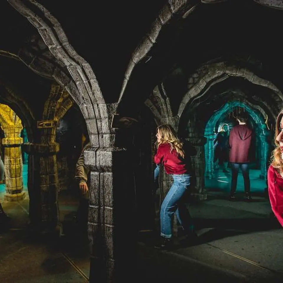 Visitors explore the atmospheric, dimly lit underground tunnels and stone archways, part of an immersive journey through Edinburgh's darkest history at The Edinburgh Dungeon attraction.