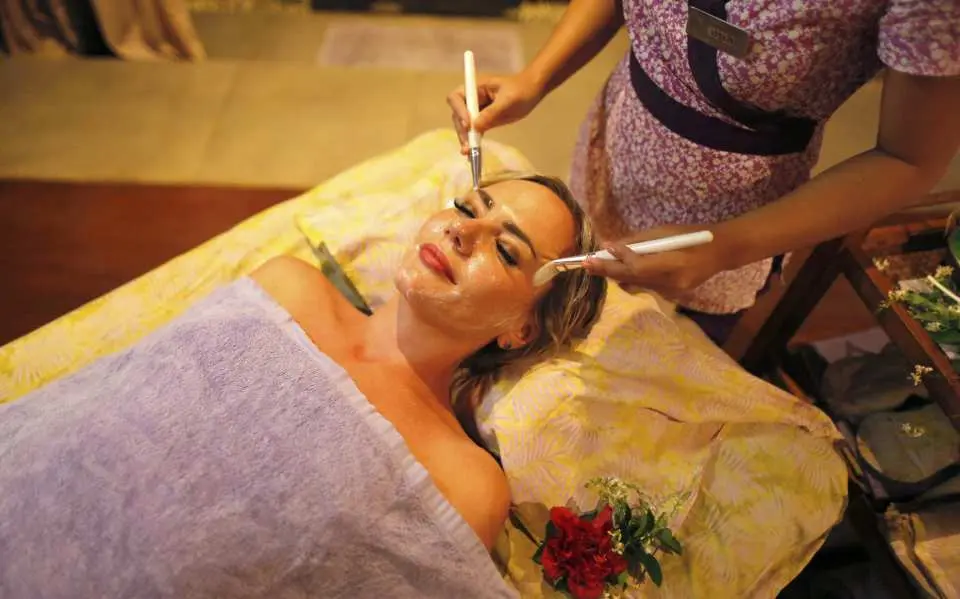 A woman experiences a luxurious facial treatment at Tirta Spa Boracay, with two therapists expertly applying a mask for rejuvenation and ultimate relaxation.