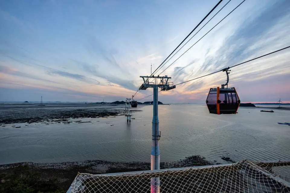Jebu Island Marine Cable Car crossing the sea at sunset, where an orange-red sky and vast tidal flats create a magnificent and romantic coastal landscape.