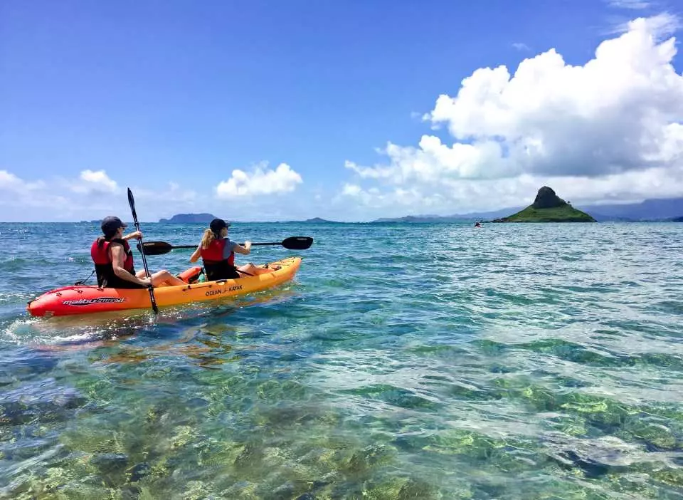 ハワイ、オアフ島で、2人の旅行者が透き通った青い海をカヤックで有名なチャイナマンズハット島へ向かい、セルフガイドのカヤック体験と美しい景色を楽しんでいます。