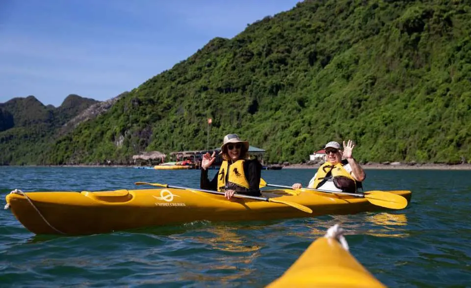 Travelers enjoy kayaking in Halong Bay's Lan Ha Bay, paddling through emerald waters to explore, with V'Spirit Cruise offering exciting water adventure activities.