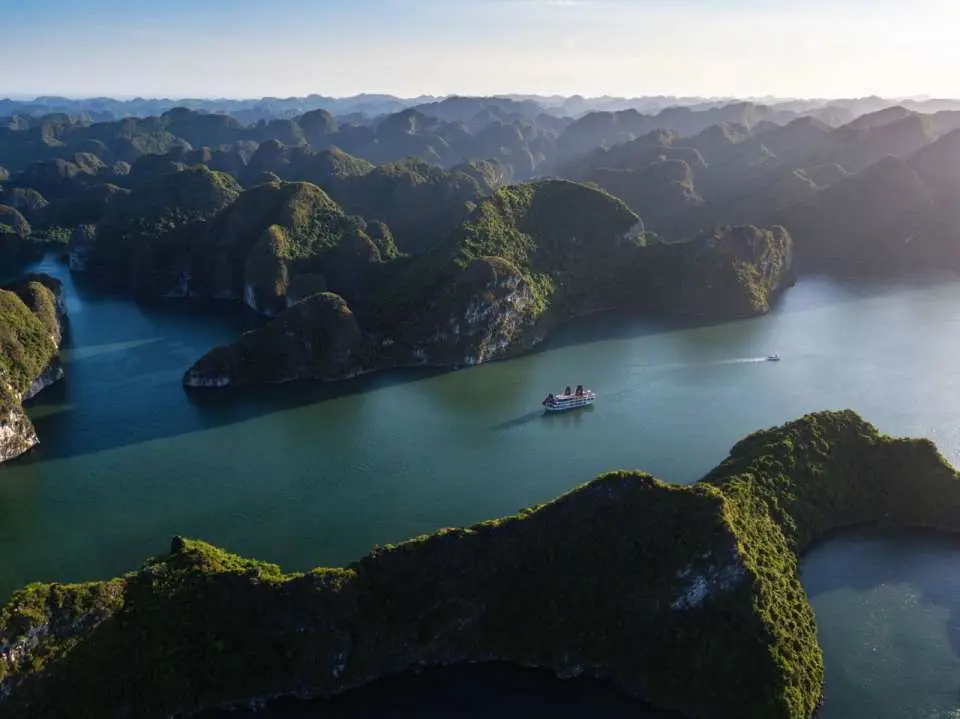 An aerial view of the magnificent karst landscape of Halong Bay and Lan Ha Bay, with the V'Spirit luxury cruise ship navigating through, offering an unforgettable Vietnamese nature adventure.