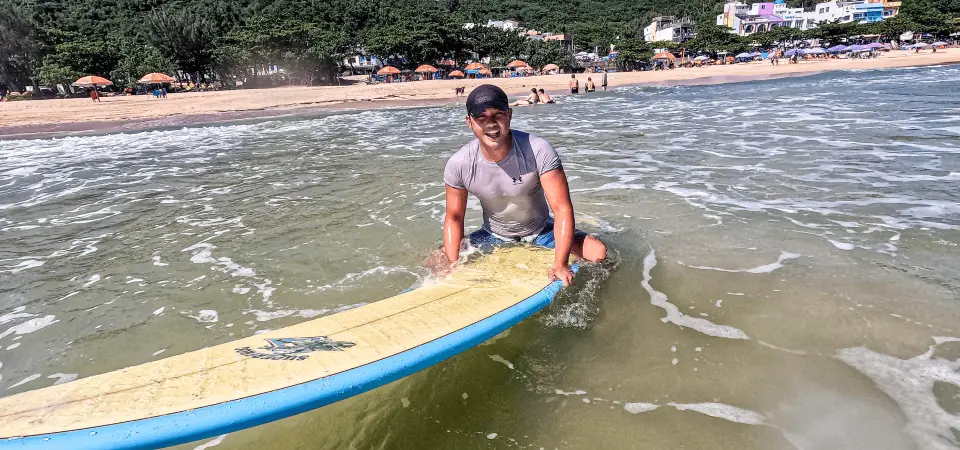 A smiling surfing instructor guiding a stable surfboard in the shallow waters of Kenting beach, ready for a fun beginner surfing lesson.