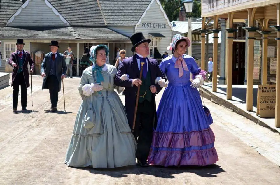 Visitors dressed in authentic 19th-century gold rush era costumes strolling down a bustling historic street at Sovereign Hill, bringing Victoria's past to life.