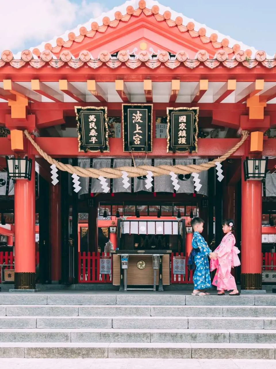 兩位穿著藍粉色和服的可愛孩童站在沖繩波上宮莊嚴的階梯前，捕捉充滿日式風情的兒童旅拍紀念照。
