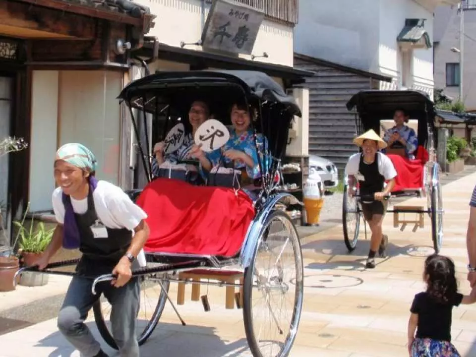 金澤東茶屋街上，兩位穿著和服的遊客乘坐人氣「羅馬屋」觀光人力車，車夫笑容滿面地帶領遊覽，體驗日本傳統風情。