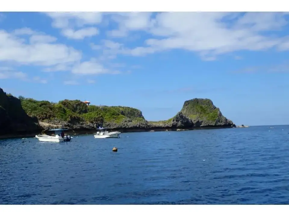 Picturesque coastal scenery of Okinawa's Onna Village, with boats moored in a tranquil blue bay against lush, rocky cliffs.