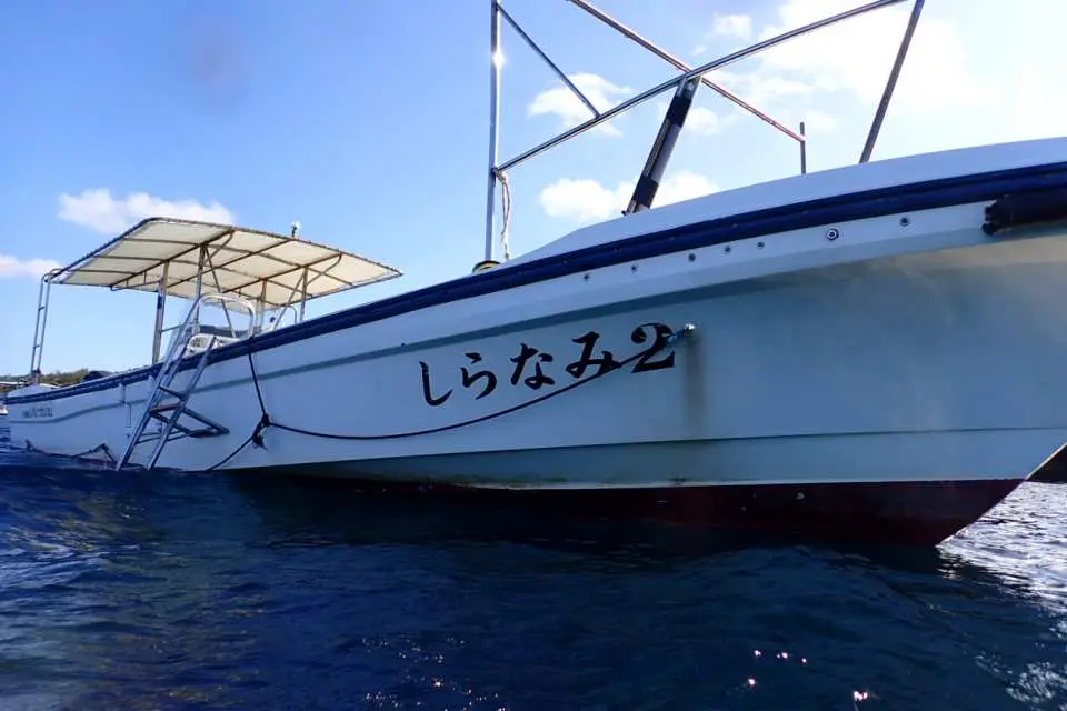 Okinawa Onna Village water activity boat 'Shiranami 2' moored on the blue sea, ready to transport visitors to the Blue Cave for snorkeling and sea walking.