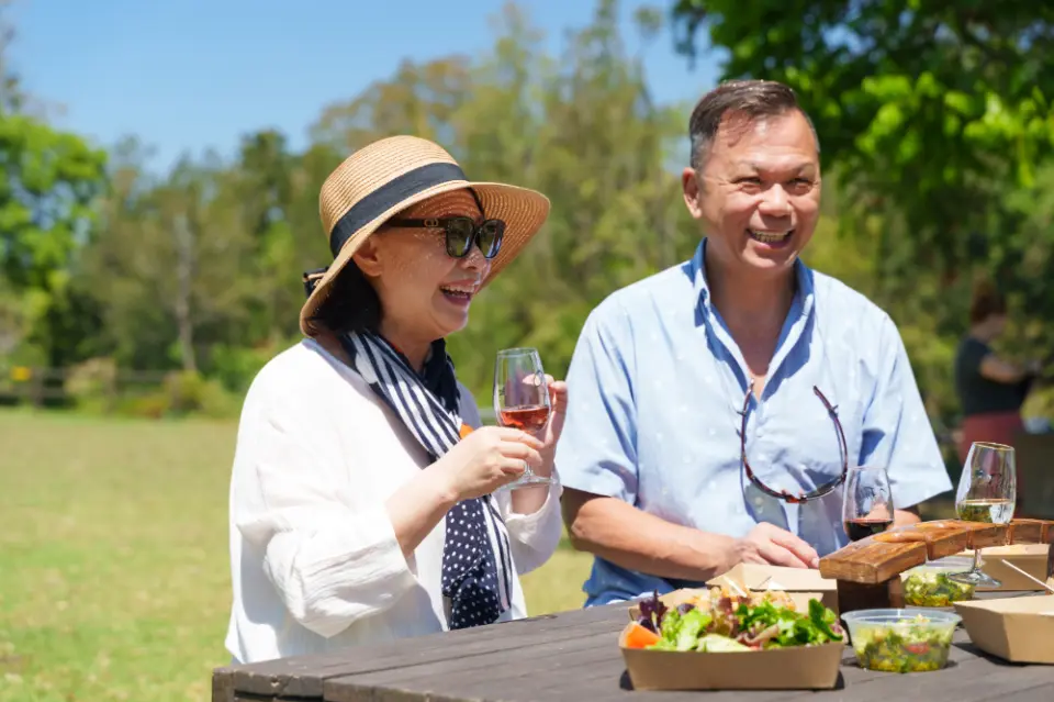 At Canungra Valley Vineyards, a couple enjoys a picnic and sparkling wine on an outdoor grassy area under the sun, showcasing a relaxed and pleasant lunch experience at the winery, savoring local fine wine.