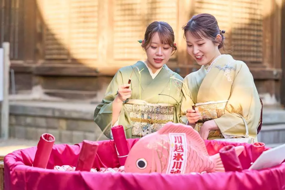 川越氷川神社で、着物姿の若い女性二人が鯛みくじを引いて楽しむ様子。和服レンタルでの文化体験を満喫。