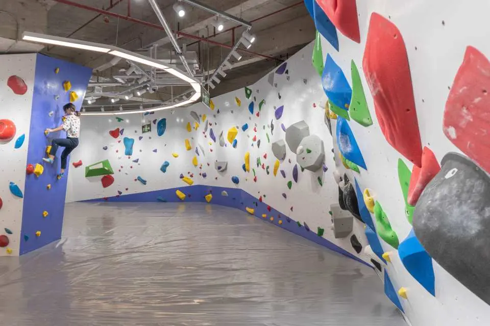 A climber challenging a blue and white bouldering wall at Banana Climbing Shenzhen, with diverse colorful climbing routes visible in the background.