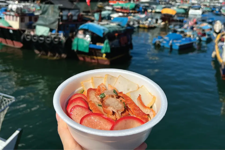A delicious bowl of authentic Sampan Noodles (艇仔粉) with BBQ pork and fish slices, enjoyed against the picturesque backdrop of Aberdeen Fishing Village.