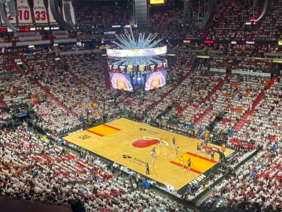 邁阿密熱火隊NBA籃球賽全景，卡西雅中心燈火通明，球員在場上奮戰，滿場球迷的歡呼聲與巨型記分板的資訊，共同構成熱鬧的比賽現場。