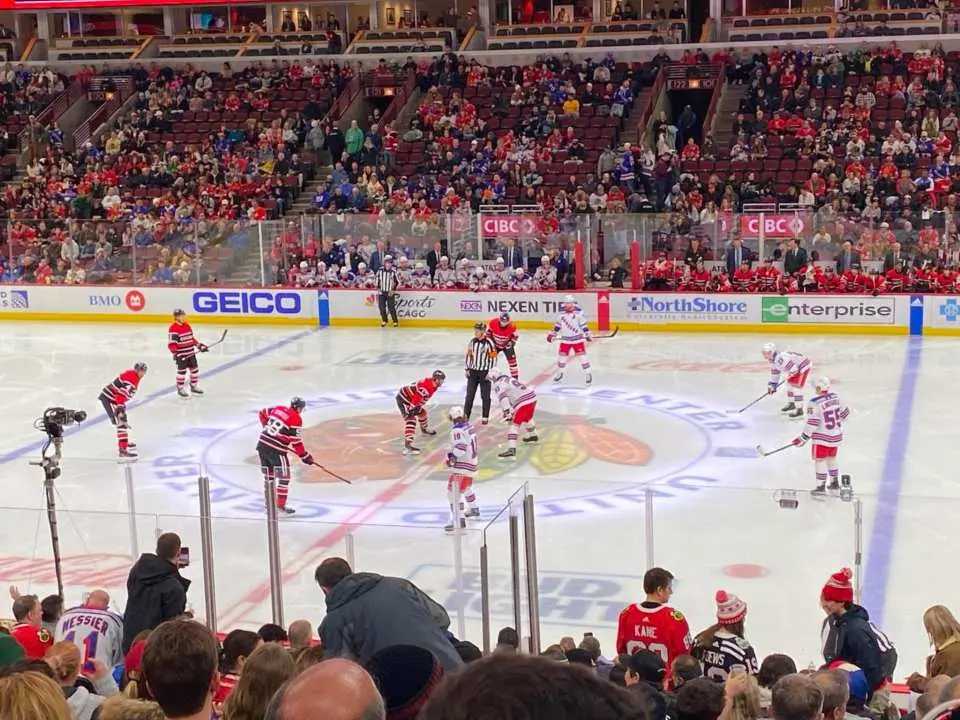 Mid-range view from the stands at United Center, capturing Chicago Blackhawks players and opponents gathered at the center face-off circle, poised for NHL game action.