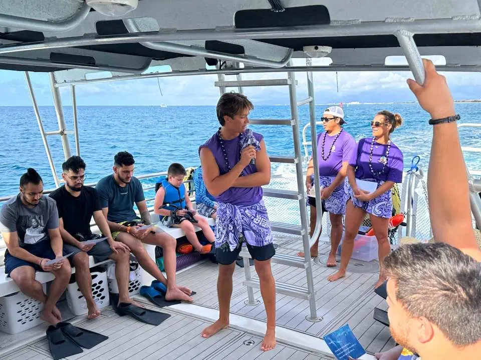 Trên thuyền lặn ngắm rùa Waikiki, Oahu, du khách chăm chú lắng nghe hướng dẫn viên giải thích hoặc thưởng thức các buổi biểu diễn văn hóa, một số người mặc trang phục đặc trưng của Hawaii.