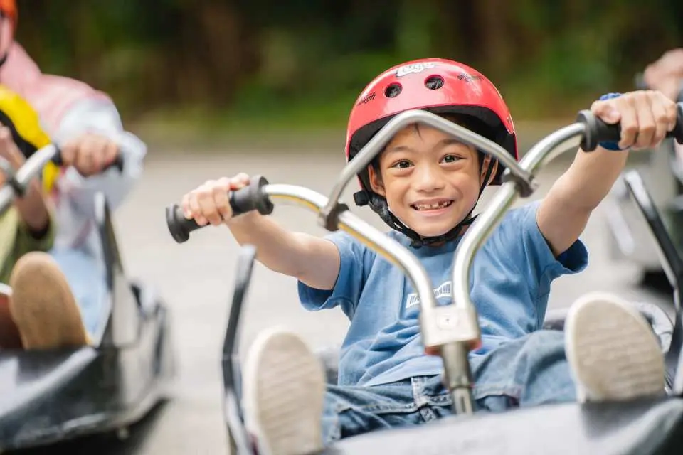 A child in a red helmet beams with a bright smile while experiencing the family-friendly and exhilarating outdoor activity of luge riding at Kuala Lumpur Skyline Luge, Malaysia.