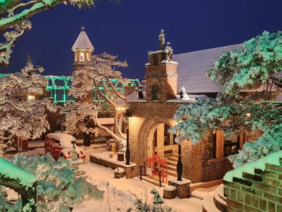 Picturesque brick buildings and towers within Yeoju's Ludensia theme park, beautifully covered in fresh snow and warmly illuminated at night, creating a magical winter atmosphere, perfect for family visits.