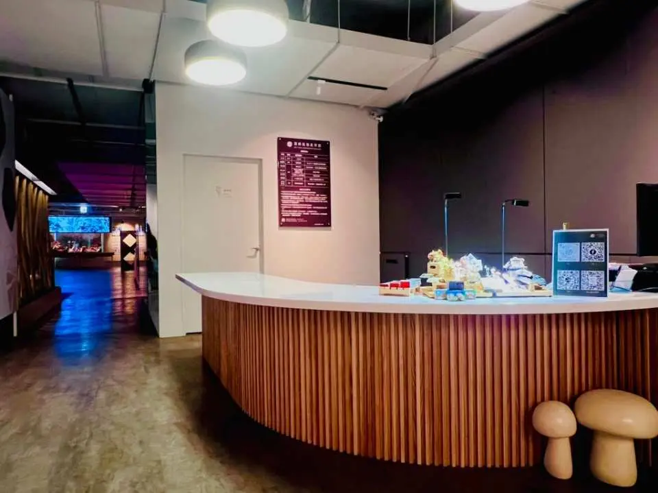 台中雾峰菇类博物馆入口处的现代化接待柜台，饰有木质纹理与可爱蘑菇摆设，提供游客咨询服务与电子凭证兑换。