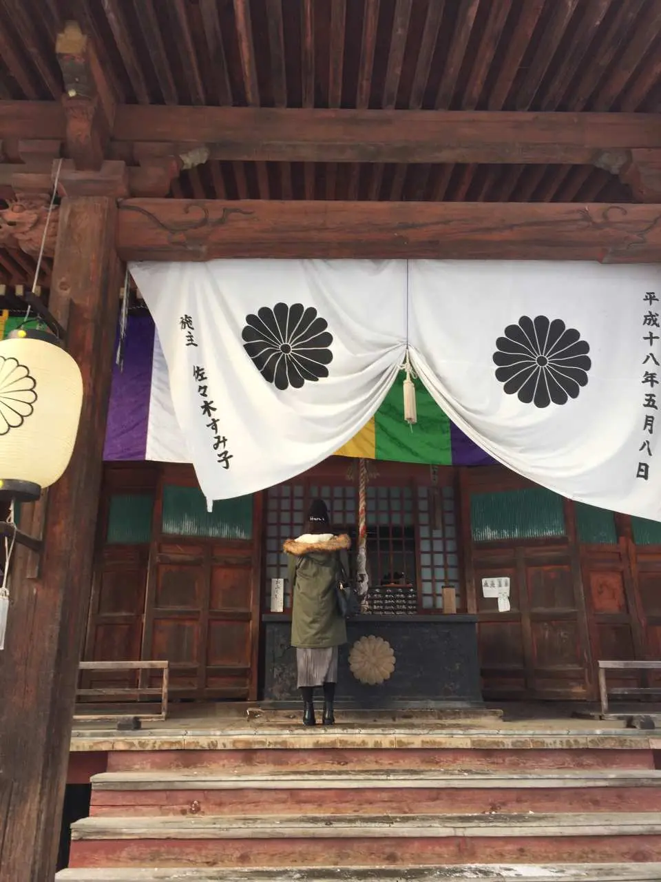 旅客站在岐阜高山傳統寺廟或神社前參拜，莊嚴的菊花家紋布幔彰顯日式文化。專業攝影記錄這份虔誠。