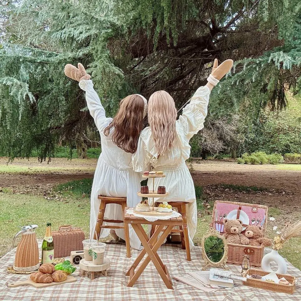 兩位穿著白色洋裝的女性在新宿御苑享受時尚可愛的日式野餐體驗，野餐墊上擺滿精緻點心與香檳。