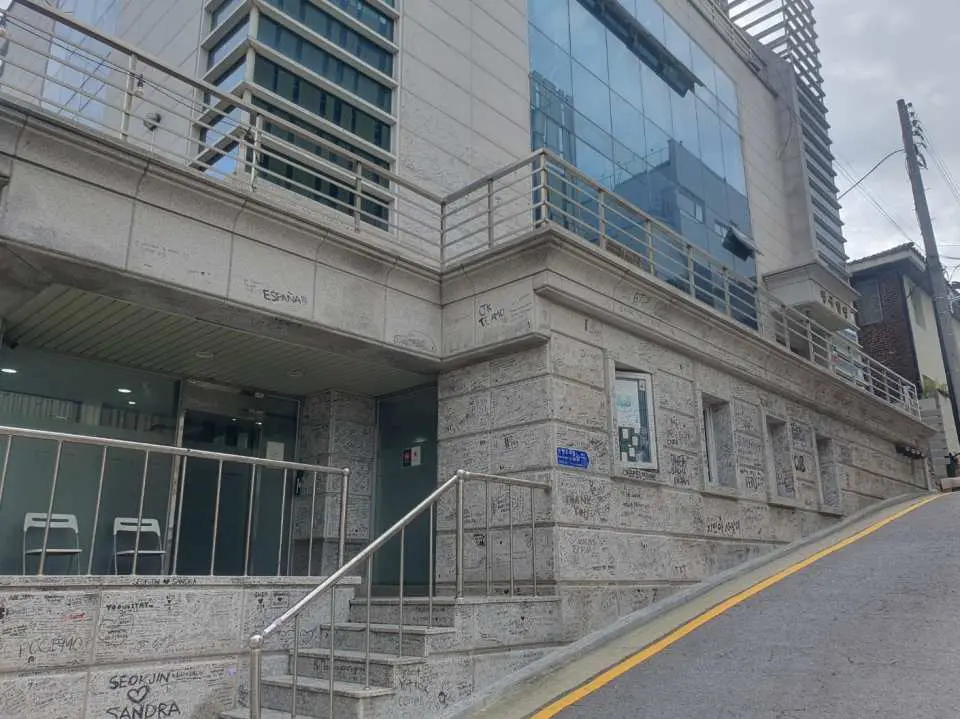 ソウルでのK-POPアイドル聖地巡礼ツアー。古い芸能事務所や宿舎のような建物で、外壁にはファンのメッセージがあり、懐かしい雰囲気が漂う。