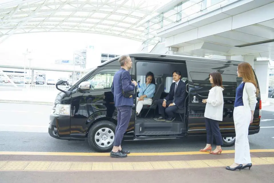 Professional driver assisting travelers boarding a spacious private transfer van at Tokyo airport, ensuring comfortable, hassle-free service to their destination.