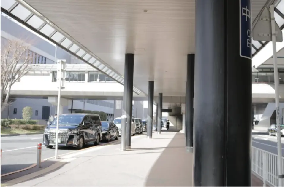 Covered transfer area at Tokyo Airport with multiple black luxury sedans or vans neatly parked, providing shelter and a comfortable waiting environment for passengers.