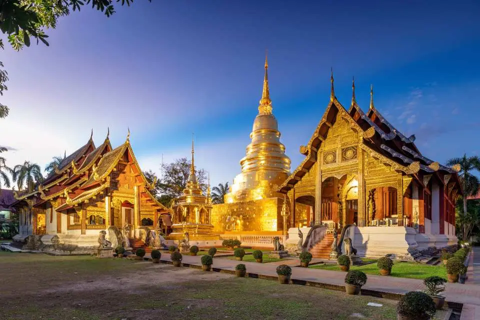 วัดพระสิงห์เชียงใหม่ยามสนธยา เจดีย์ทองอร่ามและสถาปัตยกรรมวัดส่องประกายภายใต้ท้องฟ้าสีคราม สร้างบรรยากาศยามเย็นที่สงบและศักดิ์สิทธิ์