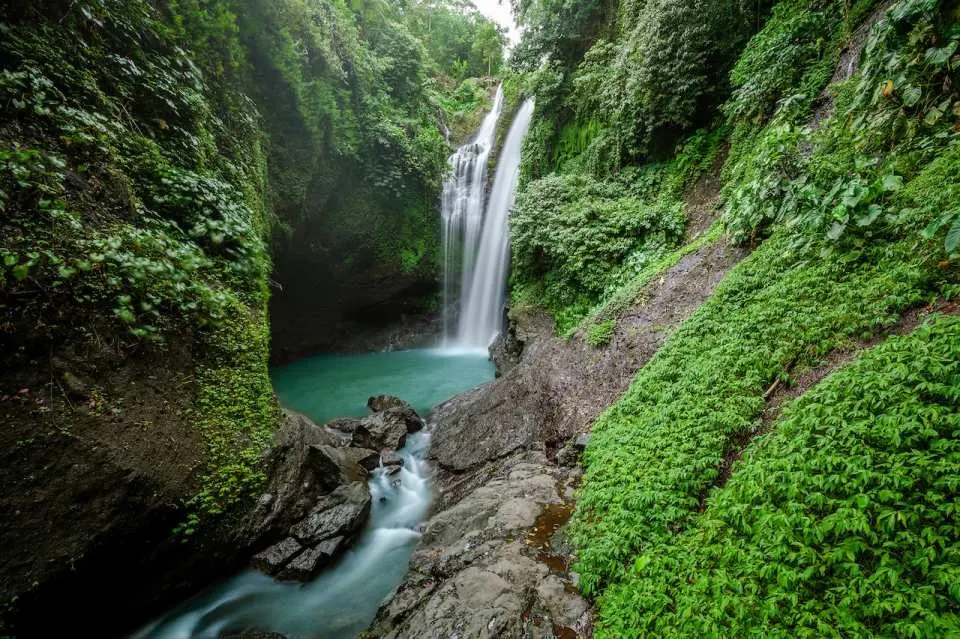 巴厘岛北部阿灵阿灵瀑布或桑班安瀑布，清澈瀑布水流注入碧绿水潭，被茂盛热带植被环绕，适合探险与浮潜。