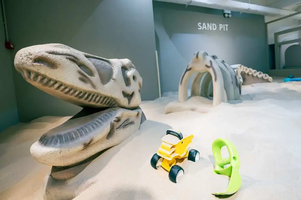大树先生的家室内沙池区，摆放着恐龙化石骨架模型和挖沙玩具，激发儿童探险乐趣。