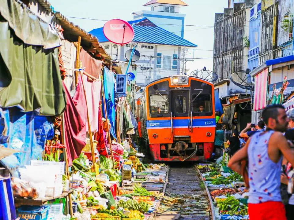 A train slowly passes through Maeklong Railway Market, with vendors' stalls right next to the moving train, offering a unique glimpse into this famous Thai market.