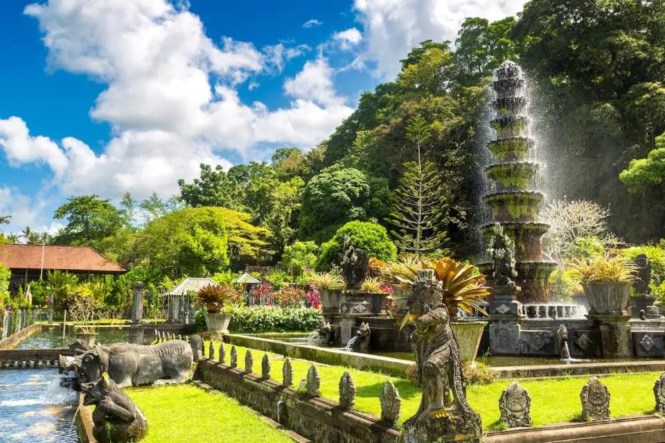 The elegant Tirta Gangga Water Palace in Bali, with its iconic tiered fountain, ornate Balinese stone statues, and serene pools set amidst vibrant tropical gardens, a royal cultural site.
