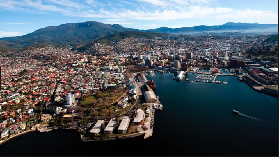 Panoramic aerial view of Hobart, Tasmania, showcasing its vibrant city skyline, bustling waterfront harbor, and the majestic Mount Wellington in the background.