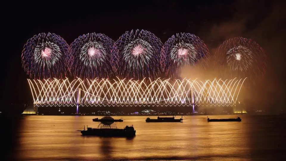 2025釜山煙火節期間，廣安大橋被獨特的金色雷射燈光圖案點綴，上方璀璨煙火綻放，海面船隻靜待。