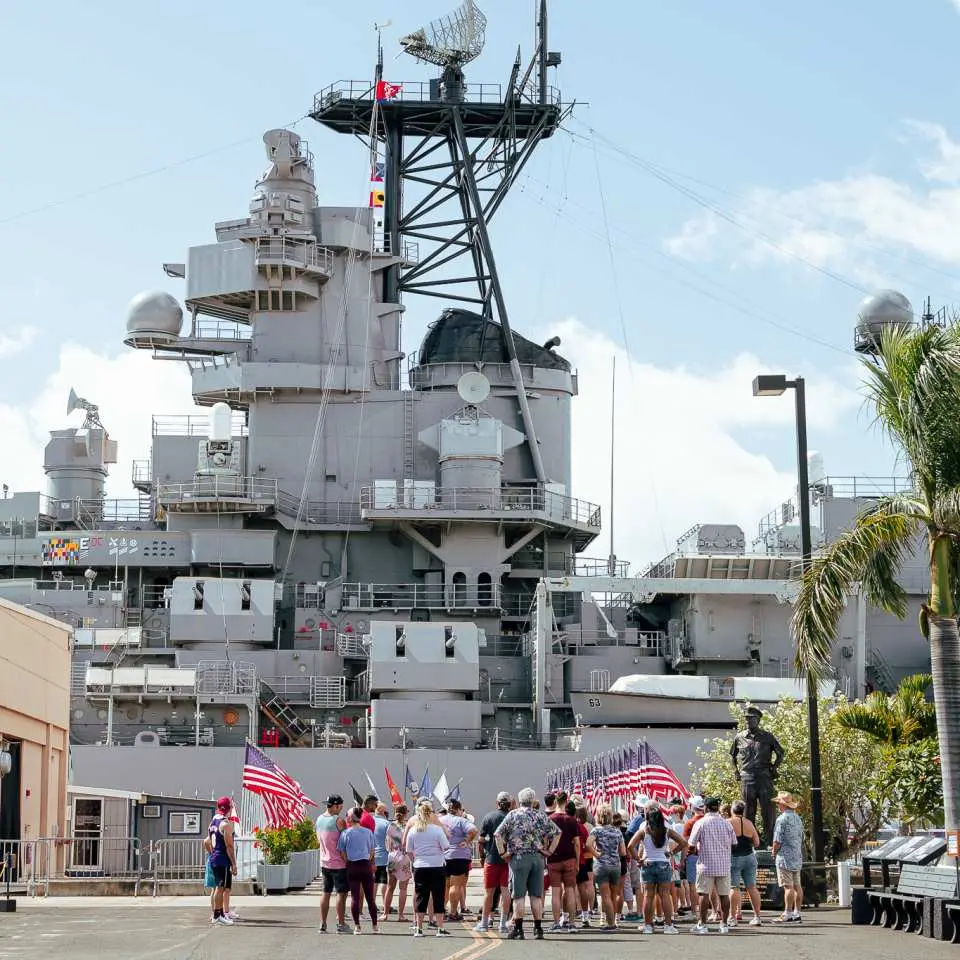 The majestic USS Missouri Battleship Memorial is docked at Pearl Harbor, Oahu, with visitors gathering in front, reflecting on its significant role in World War II history.